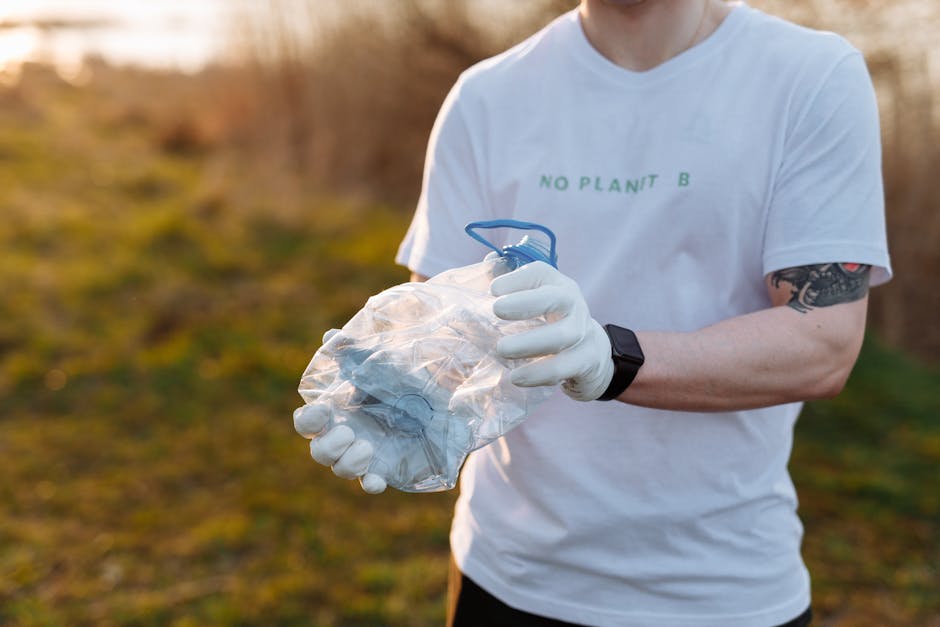 A person wearing a white T-shirt with the words 'NO PLANT B' printed in green, white gloves, and a black wristwatch is holding a clear plastic bag filled with crumpled paper or lightweight waste. The 